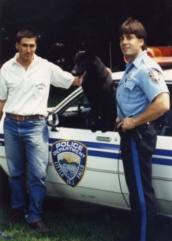 צמד שוטרים עומדים ליד ניידת ומהחלון מציץ כלב שחור- אילוף כלבים, פנסיון כלבים
