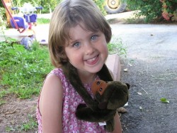 ילדה קטנה מחייכת עם בובה של קוף תלויה עליה- אילוף כלבים, פנסיון כלבים
